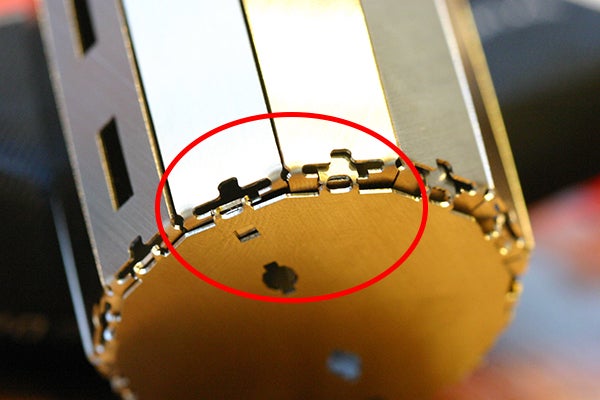 専用の冶具と手だけで組立てられるよう、随所に工夫が凝らされている。写真はロボットの胴体の底部分。底パーツをはめただけ（赤枠内右側）だとすぐ取れてしまうので、冶具の先端で底パーツのツメを内側に押し込み、引っ掛けて固定する（左側）